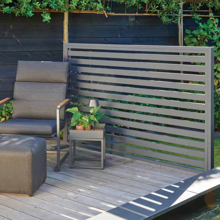 Aluminum Room Divider Accessory Shelf shown outdoors with chair, plant, and pouf on wooden deck beside modern divider panel.