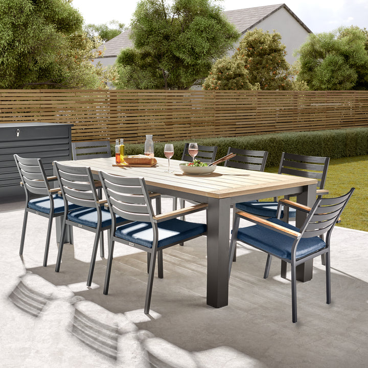 Elba 9-Piece Dining Set Spectrum Indigo with teak table, charcoal aluminum frame, and stackable cushioned chairs outdoors.