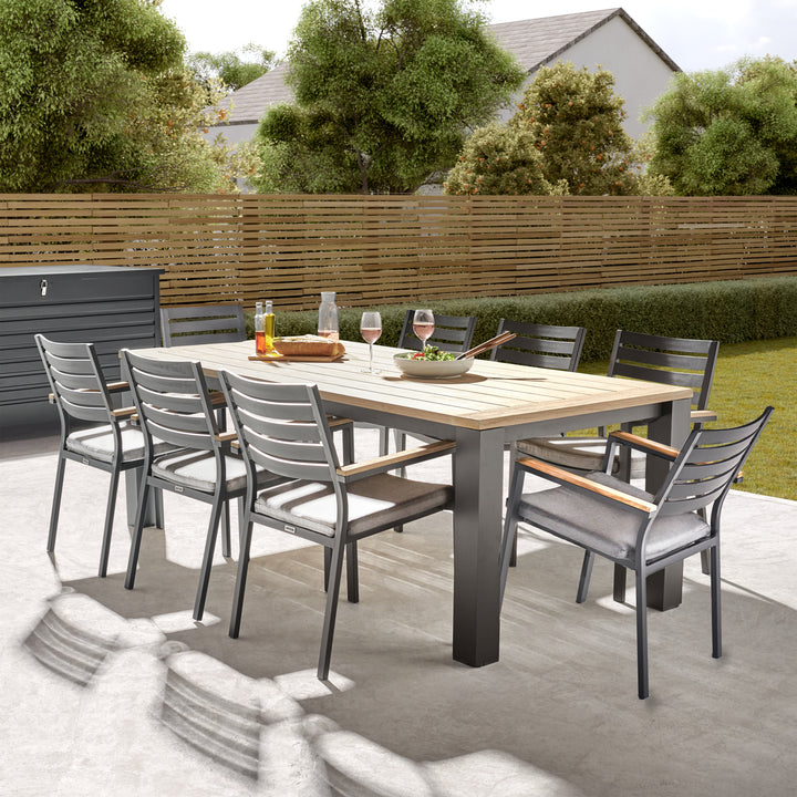 Elba 9-Piece Dining Set with teak tabletop, charcoal aluminum frame, and eight cushioned stackable chairs outdoors.