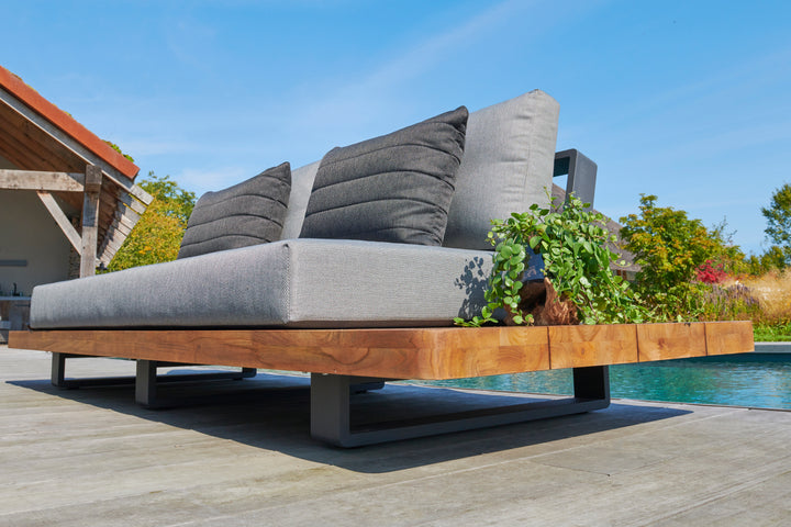 Fitz Roy Teak Sofa with natural teak, aluminum frame, charcoal cushions, and integrated side tables by a pool on deck.