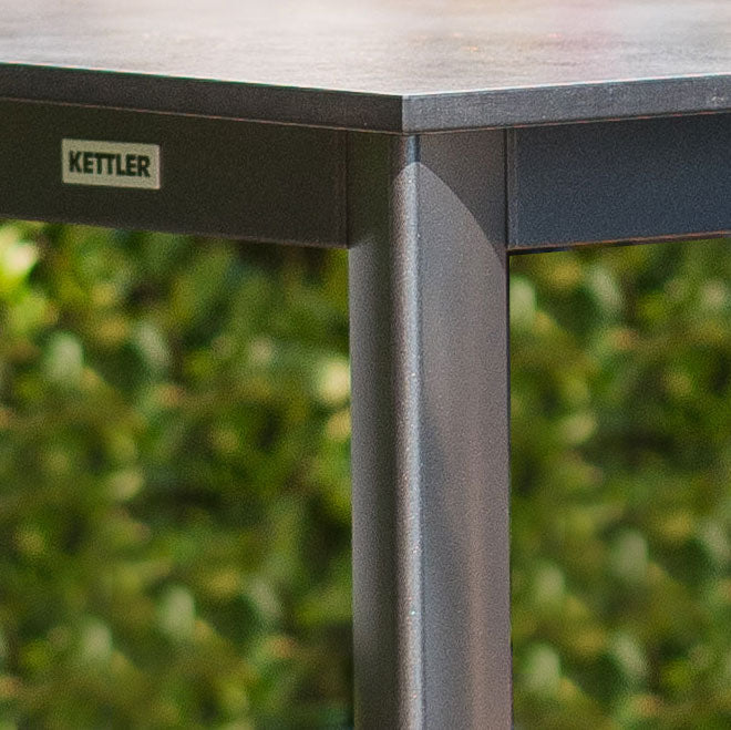 Loft HPL Dining Tables close-up of weatherproof iron gray aluminum frame and textured beveled HPL tabletop outdoors.