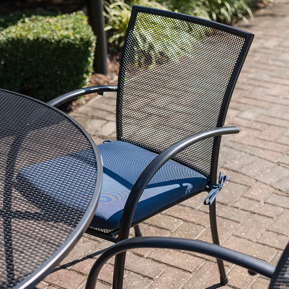 Pilano 7-Piece Round Wrought Iron Dining Set with mesh chairs and blue seat cushions on brick patio outdoors
