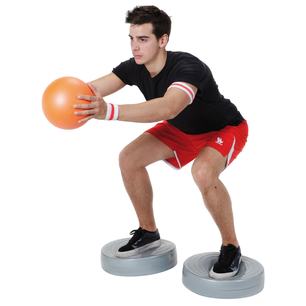 Man exercising balance and posture using Gymnic Stability Wheel and holding an orange ball in workout attire.