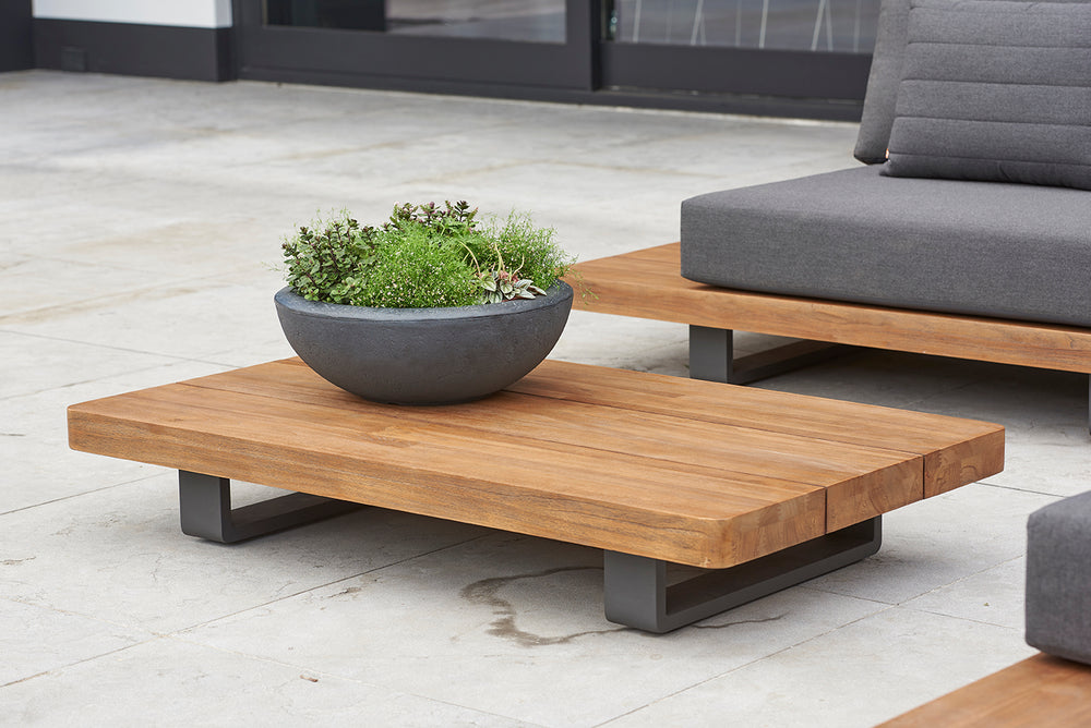 Fitz Roy 55x32x10-inch Teak Coffee Table with robust teak top and lava aluminum frame on outdoor patio setting.