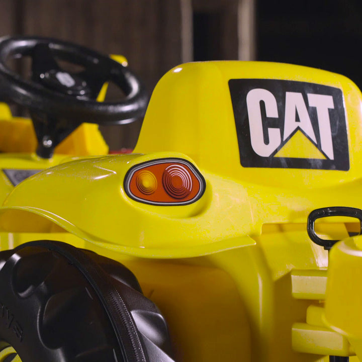 Close-up of yellow CAT Kid Tractor With Trailer showing logo, steering wheel, and front loader details.