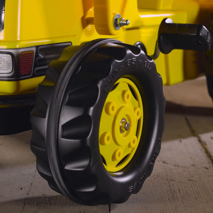 Close-up of oversized resin tire with rubber tread on CAT Kid Tractor With Trailer pedal tractor in yellow color.