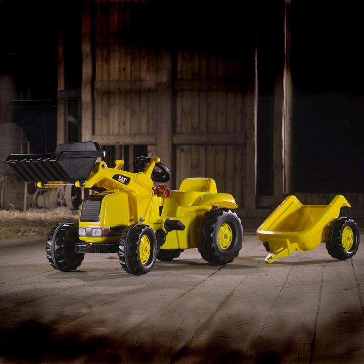 CAT Kid Tractor With Trailer pedal-powered yellow kid’s tractor with front loader and detachable trailer indoors on wood floor.