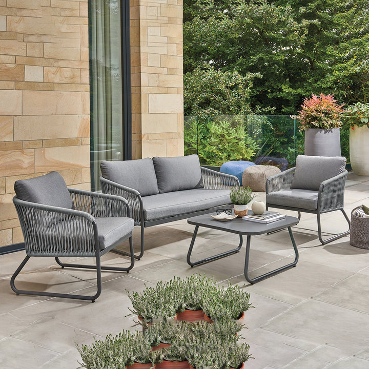 Kingston Aluminum Lounge Set with charcoal frame and cast slate cushions on a patio with greenery background.