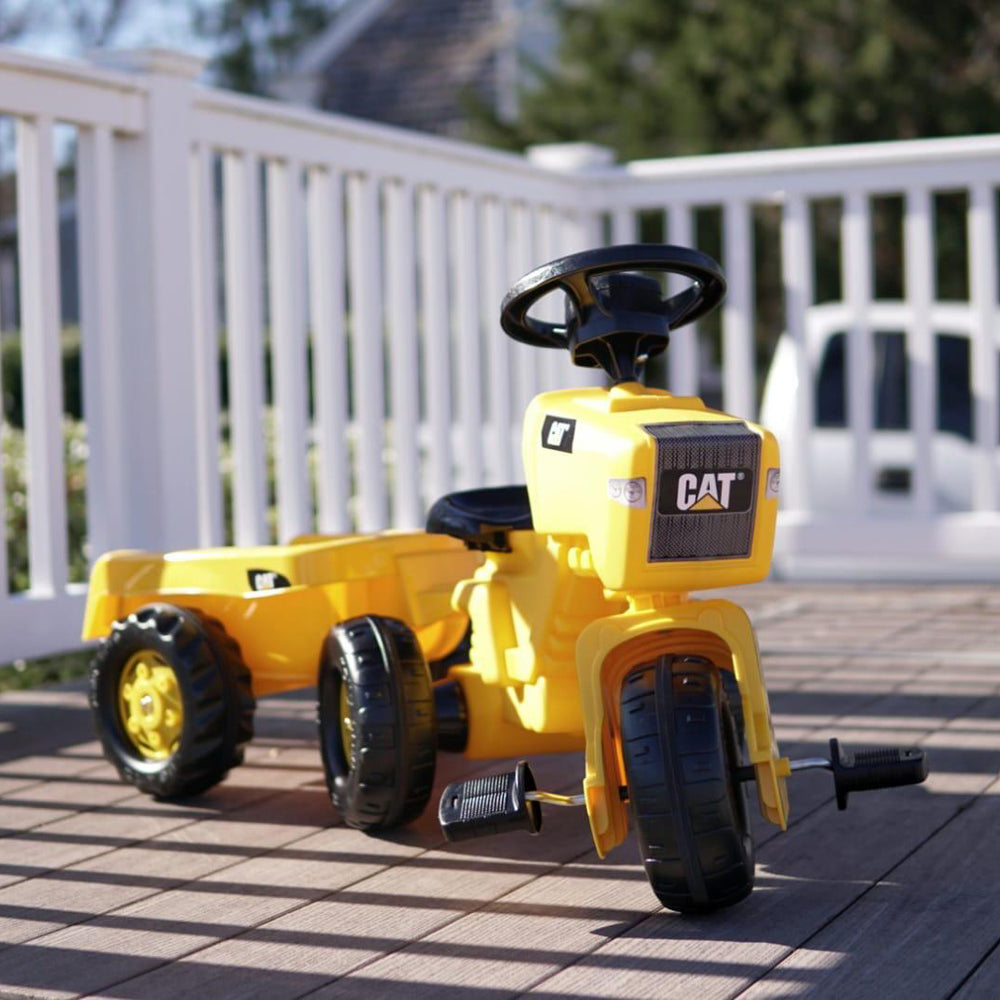 CAT 3-Wheeled Pedal Tractor With Trailer in yellow with oversized tires and removable hauling trailer on wooden deck.