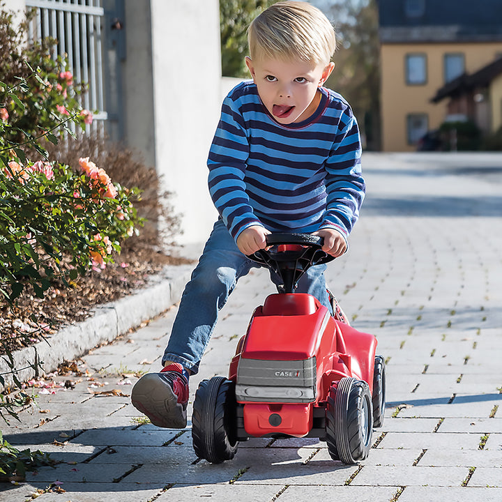 Young child riding a red Case IH Minitrac toy tractor with sturdy tires and a realistic design outdoors.