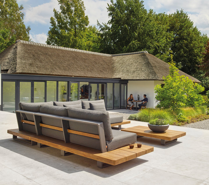 Fitz Roy Teak Corner Set modern outdoor lounge with teak wood, aluminum frame, and charcoal cushions on patio.