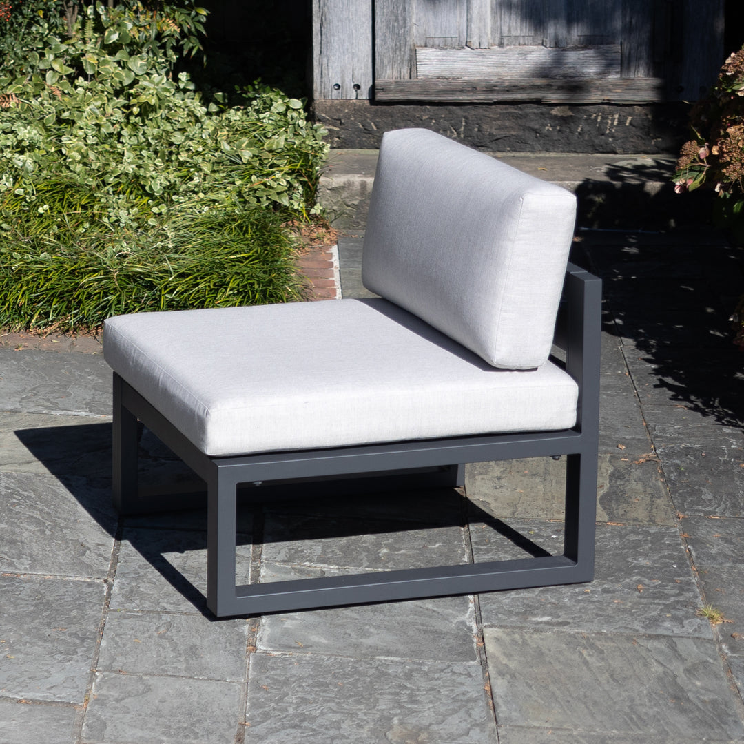 Elba Comfort Armless Chair with charcoal aluminum frame and cast silver weather-resistant cushions on stone patio.