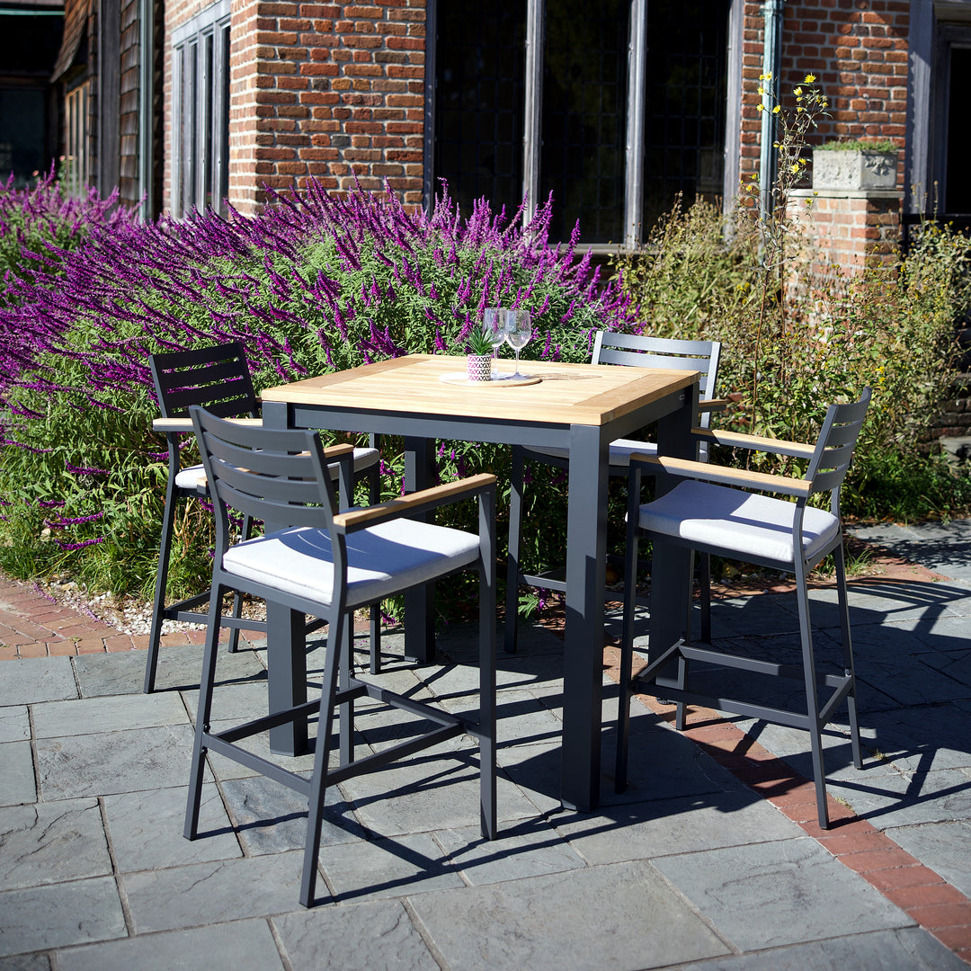 Elba Aluminum Bar Chair With Cushion in charcoal frame and teak arms around outdoor dining table with cast silver cushions.