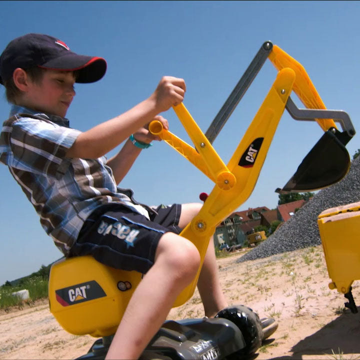Child using CAT Ride-On Digger with working levers and 360-degree rotation on a sunny day outdoors.