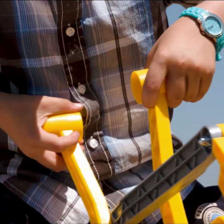 Child using dual action levers on CAT Ride-On Digger with yellow handles and plaid shirt outdoors.