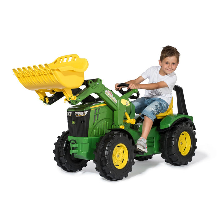 Child riding the John Deere Premium X-Trac with Loader toy tractor with functional front loader in action