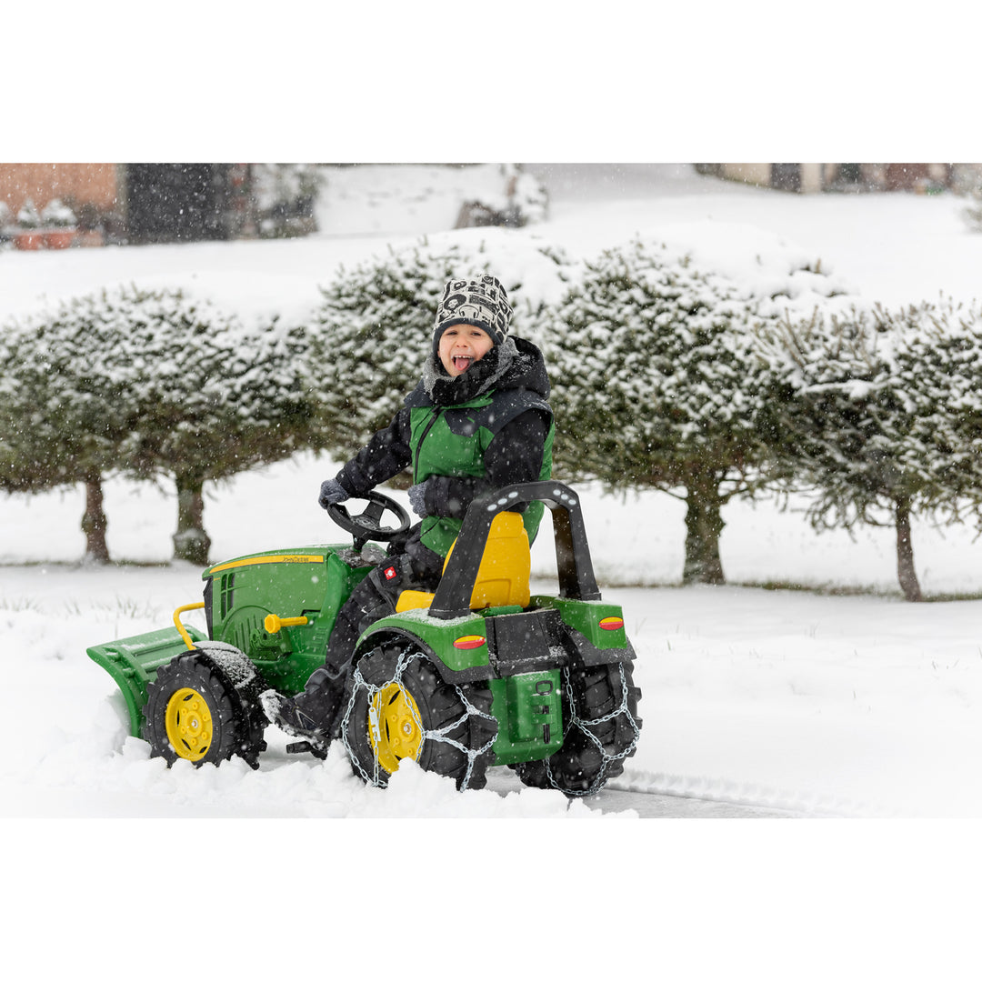 Child riding John Deere Premium X-Trac with Loader toy tractor in snowy outdoor setting with tire chains.