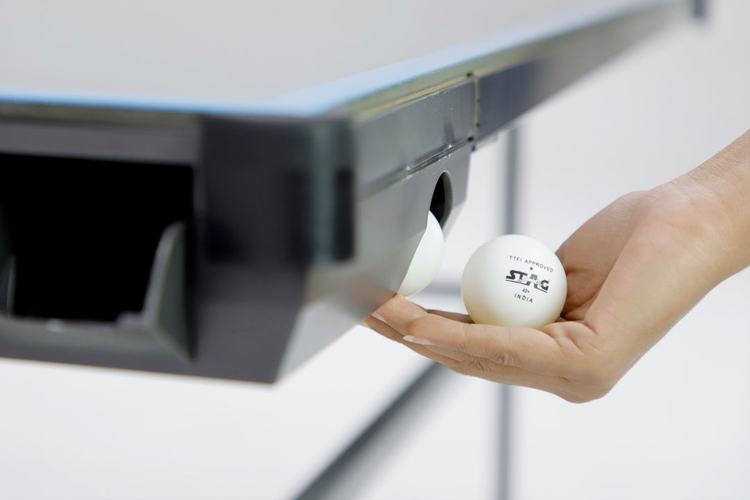 Hand holding white table tennis ball near the ball holder on the side of a blue ping pong table
