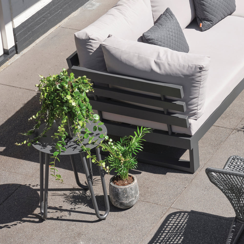 Blixum Aluminum Side Table in lava frame next to gray outdoor sofa with cushions and potted plants on patio.