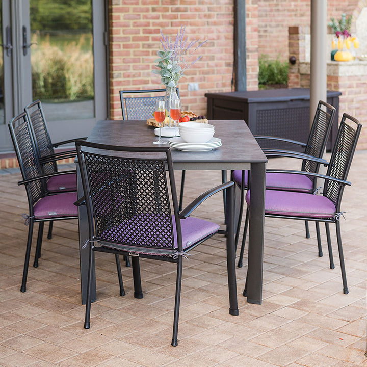 Reno 7-Piece Dining Set with wrought iron frame, six purple cushioned arm chairs, and a rectangular dining table outdoors.