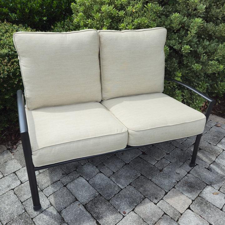 Reno Deep Seating Loveseat With Cushions in iron grey frame with sand-colored cushions on stone patio outdoors.
