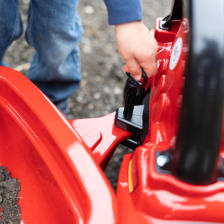 Child connecting trailer to red CASE IH Tractor With Trailer on gravel surface outdoors.