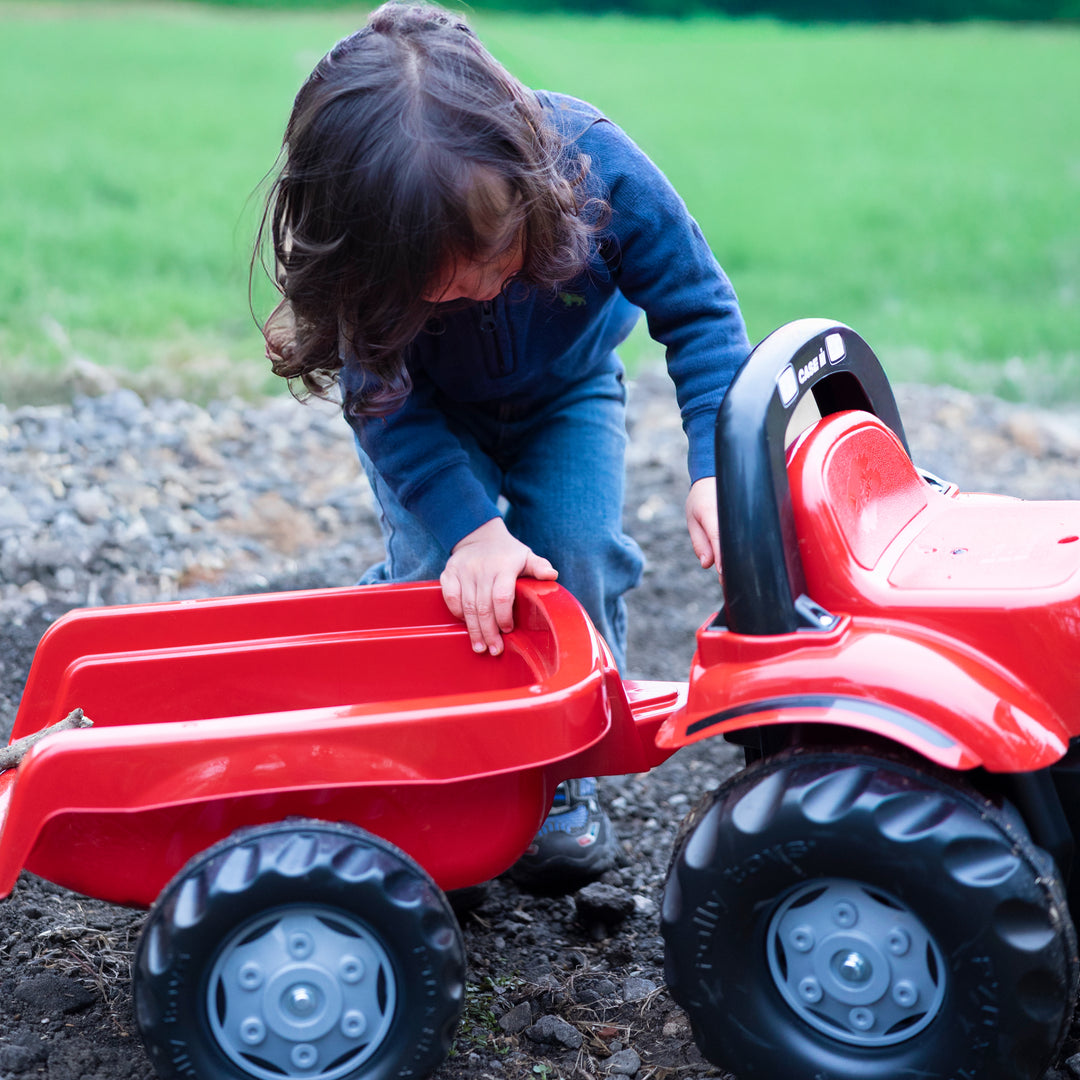 Child playing with red Case IH Tractor With Trailer on dirt outdoors fostering imagination and motor skills development.