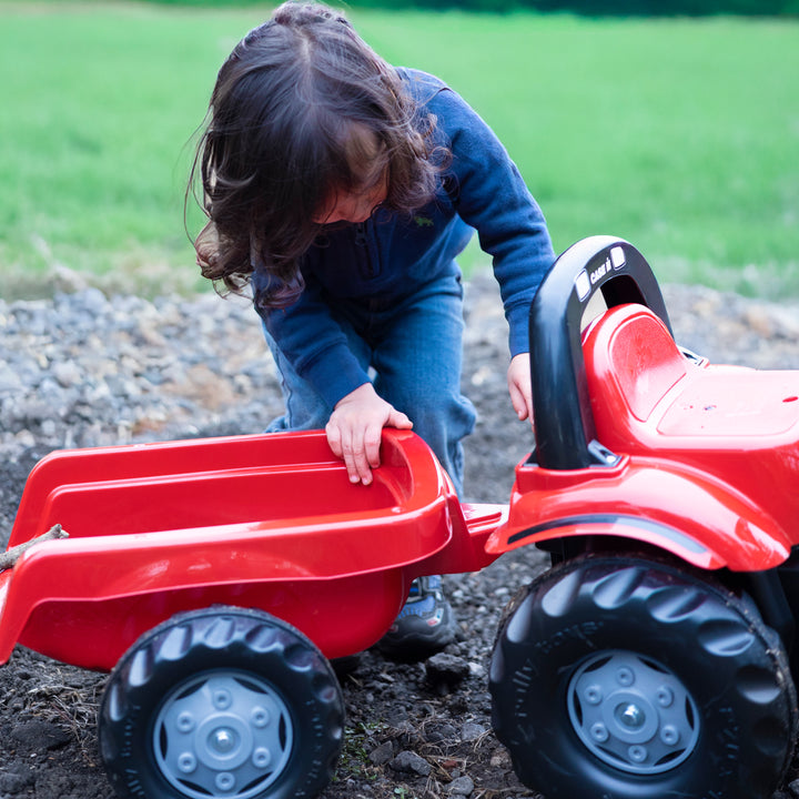 Child playing with red Case IH Tractor With Trailer on dirt outdoors fostering imagination and motor skills development.
