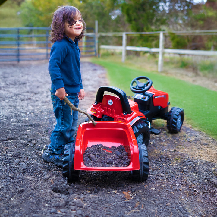 Child playing outdoors with red Case IH Tractor With Trailer filled with soil on a dirt path.
