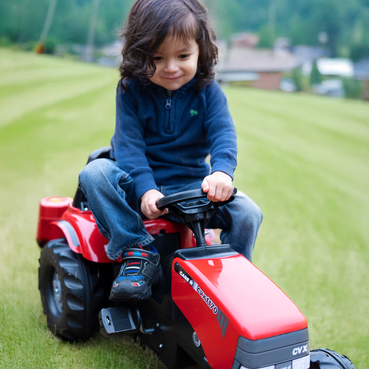 Child riding a red Case IH Tractor With Trailer on grass, enjoying outdoor play and imaginative fun.