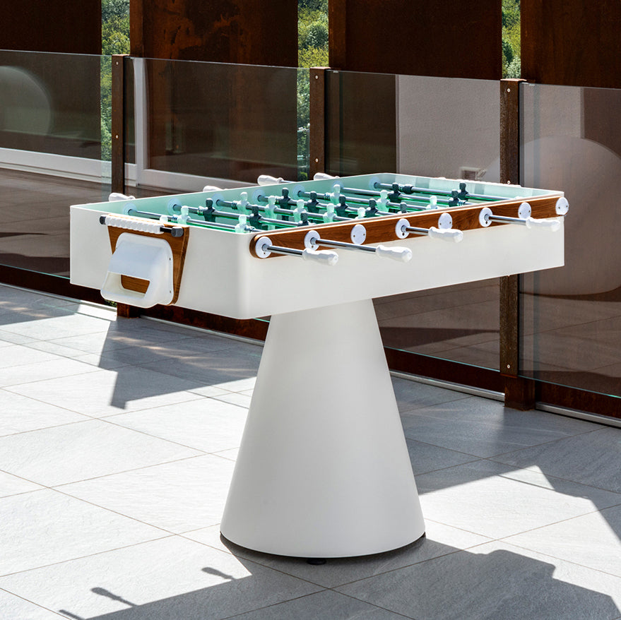 Ciclope Foosball Table with Entertainment Top & Premium Cover in white with teak trim and conical base outdoors.