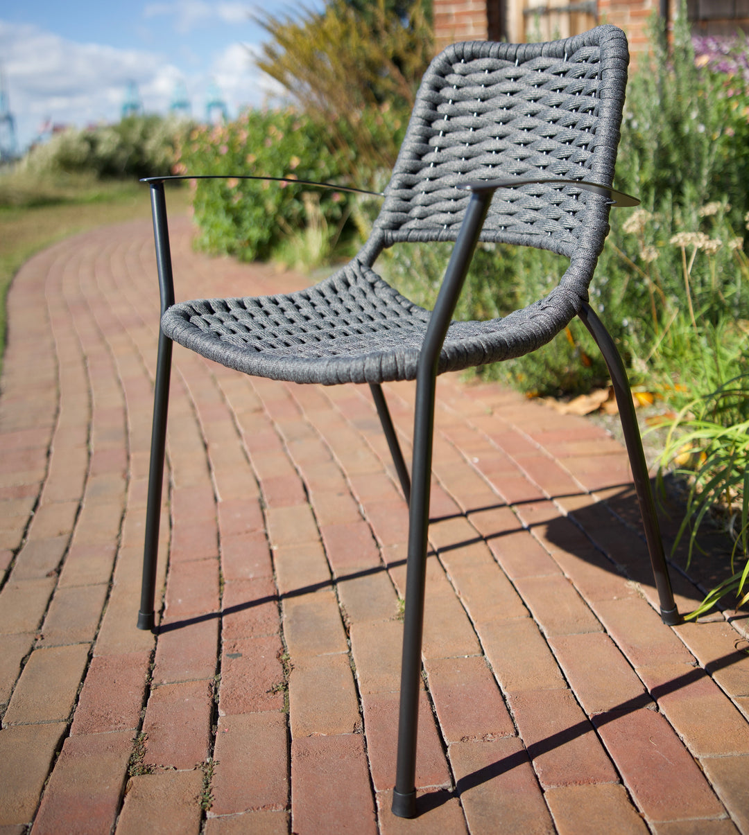 Metro Rope Stackable Arm Chair with gray weather-resistant rope weave and iron gray frame on brick pathway outdoors