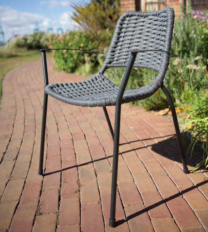 Metro Rope Stackable Arm Chair with gray weather-resistant rope weave and iron gray frame on brick pathway outdoors