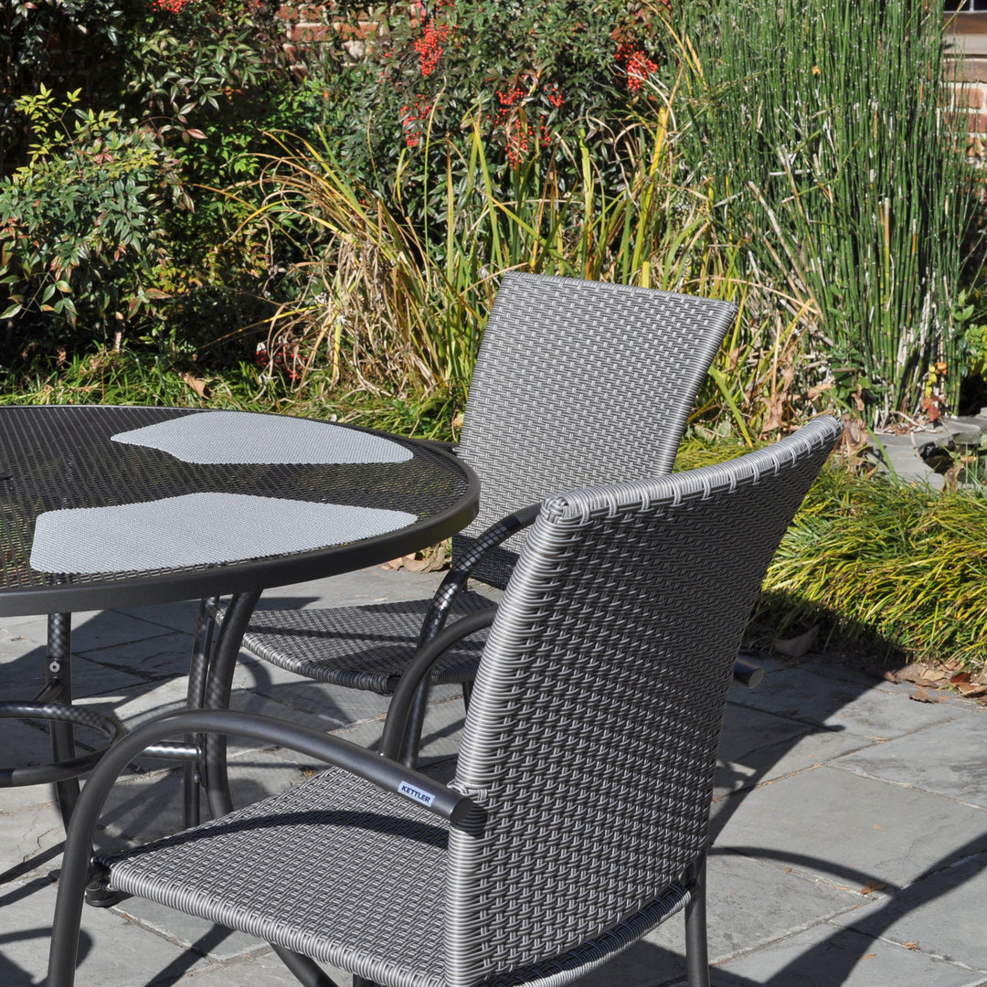 Pilano Woven 5-Piece Wrought Iron Dining Set with silver grey woven chairs and 48-inch round mesh table outdoors.