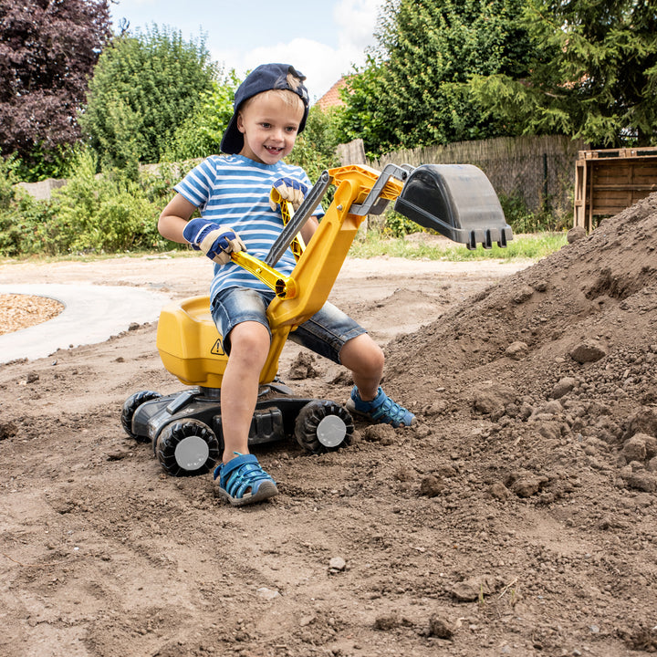 Child operating the CAT Ride-On Digger with dual action levers and rotating shovel on dirt mound outdoors.