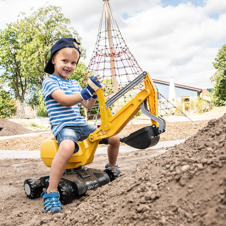 Young boy playing outdoors on yellow CAT Ride-On Digger with working shovel and rolling wheels in playground.
