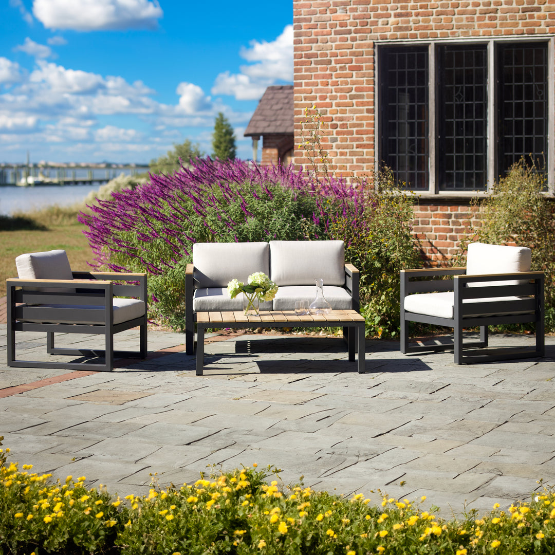 Elba Comfort Lounge Set with teak accents featuring charcoal aluminum frame and cast silver Sunbrella cushions on patio