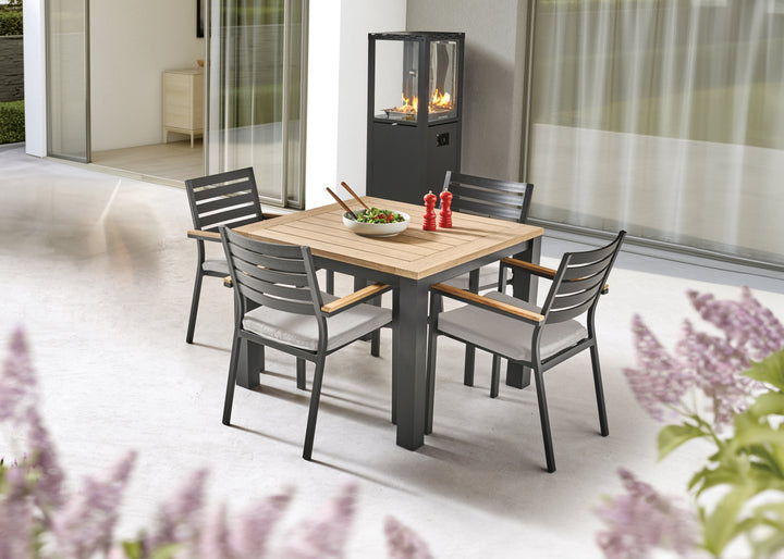Elba 5 Piece Aluminum & Teak Dining Set w 40-inch Dining Table on patio with cushions and fire pit nearby