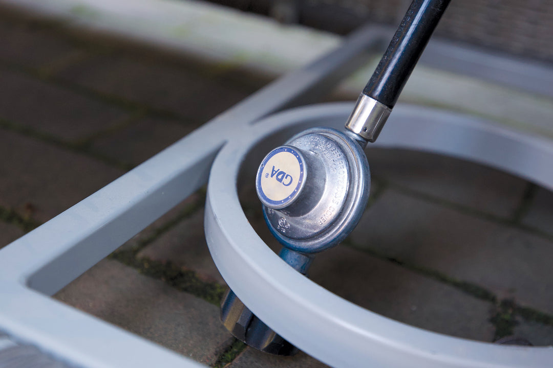 Close-up of the Palma Fire Table's propane connection and aluminum frame on a brick patio surface.