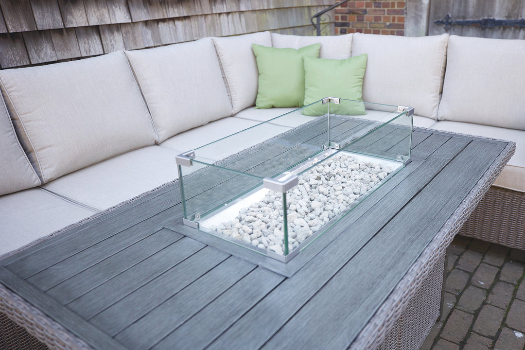 Palma Fire Table with brushed aluminum slat top, tempered glass wind guard, and lava rocks in outdoor seating area.