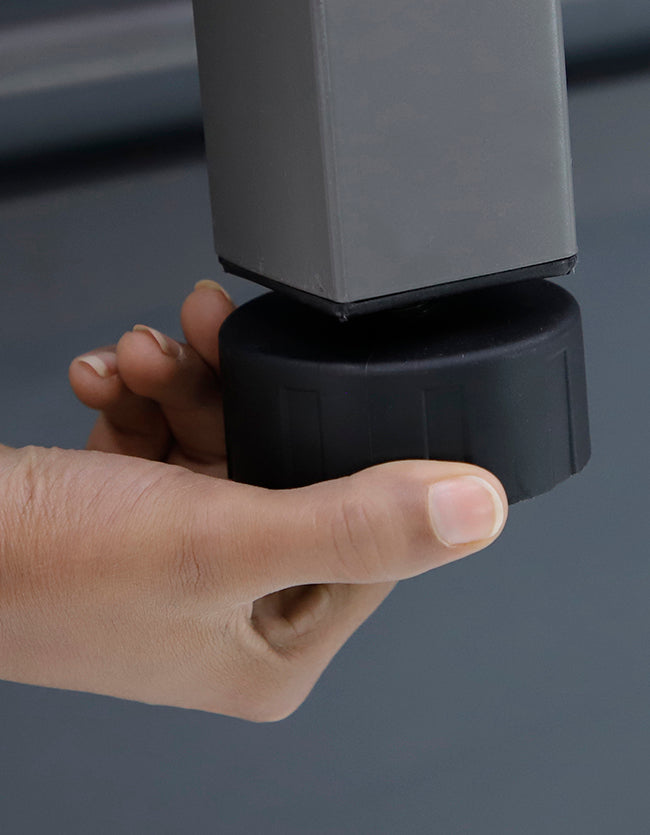 Hand adjusting black plastic furniture glide attached to square grey metal leg on smooth floor surface