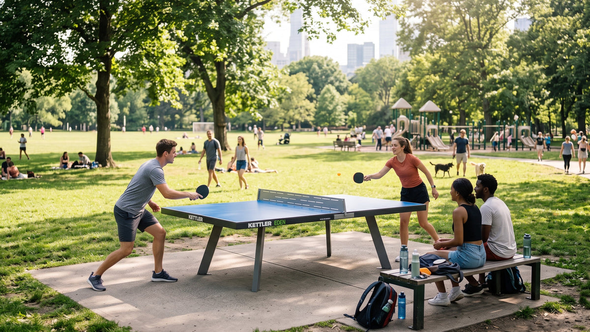 People playing table tennis in a sunny city park with spectators seated nearby and a playground in the background