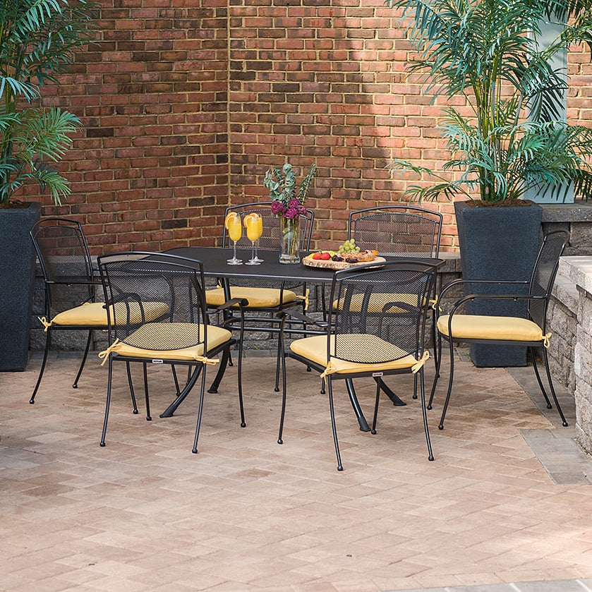 Henley Wrought Iron Mesh Stackable Arm Chair - Set Of 6 arranged around a table with yellow cushions in a patio setting.