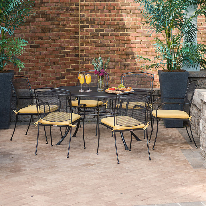 Henley Wrought Iron Mesh Stackable Arm Chair - Set Of 6 arranged around a table with yellow cushions in a patio setting.