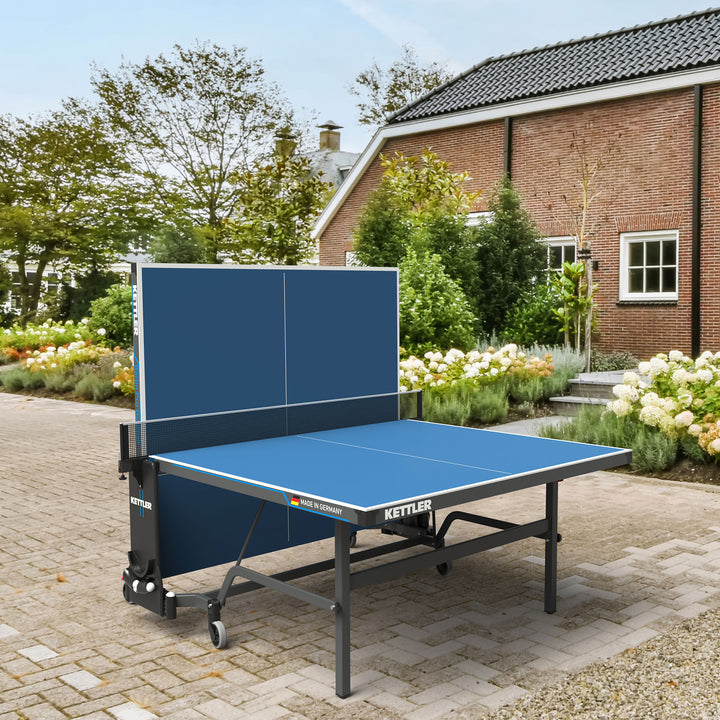 Berlin Pro Outdoor Table Tennis Table 4-Player Bundle with weatherproof top, permanent net, and storage wheels outside a house.