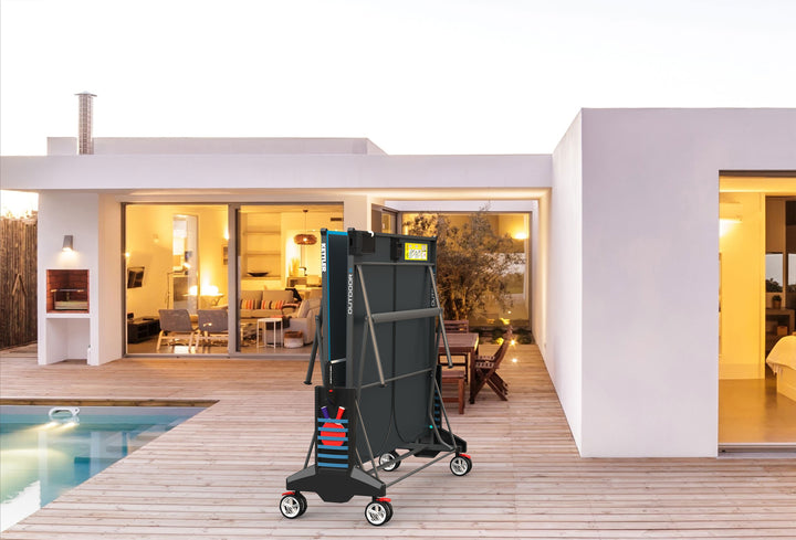 Outdoor 6 Table Tennis 4-Player Bundle folded for compact storage on a wooden patio outside a modern house.