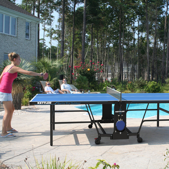 Berlin Pro Outdoor Table Tennis Table 4-Player Bundle in backyard setting with players enjoying a game near a pool.