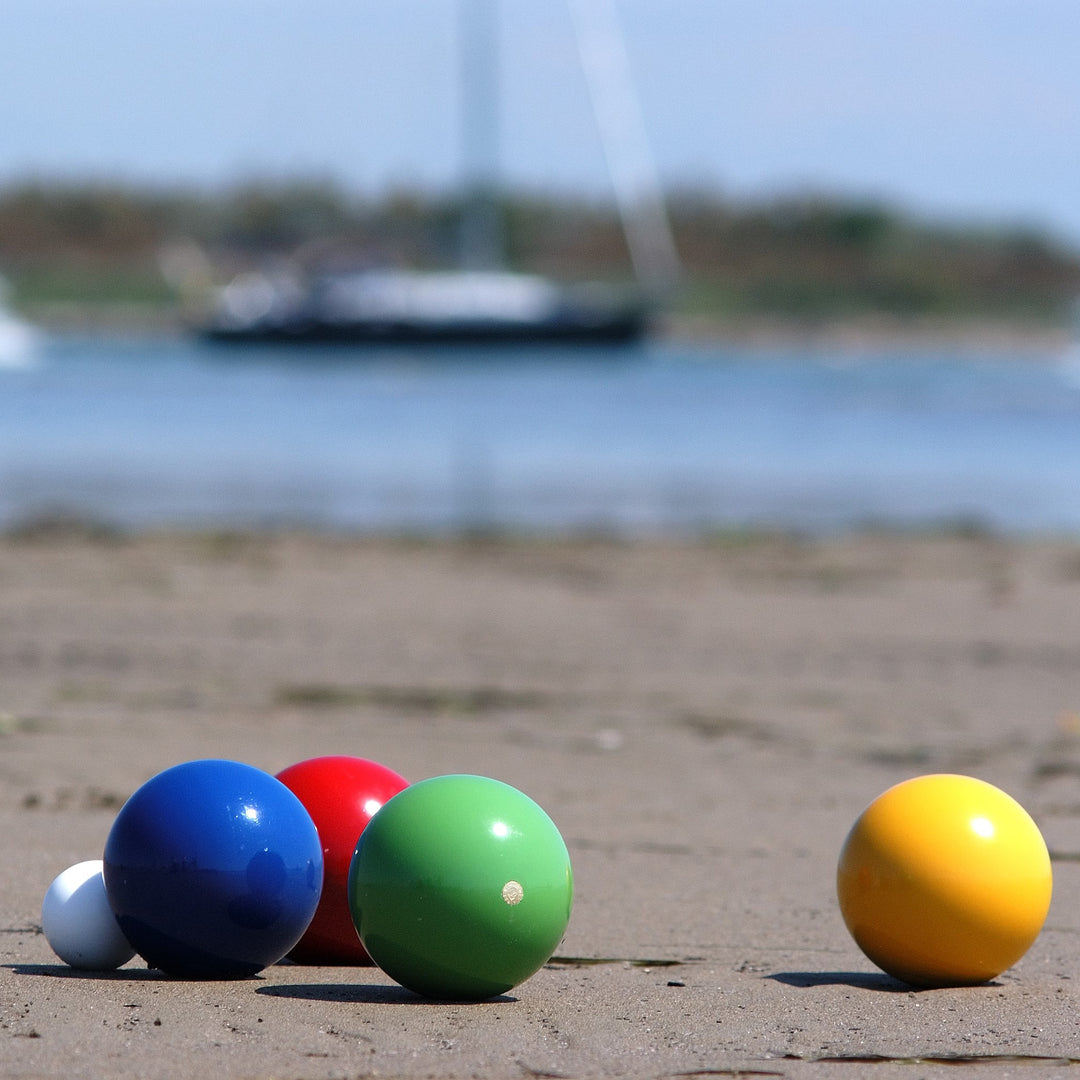 Junior Bocce Set showing colorful bocce balls on sand with water and a boat blurred in the background.