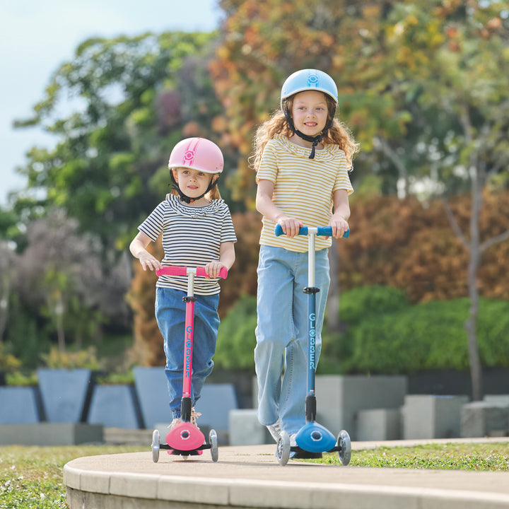 Two kids wearing helmets riding Elite Scooter models in aqua and fuchsia outdoors on a sunny day.