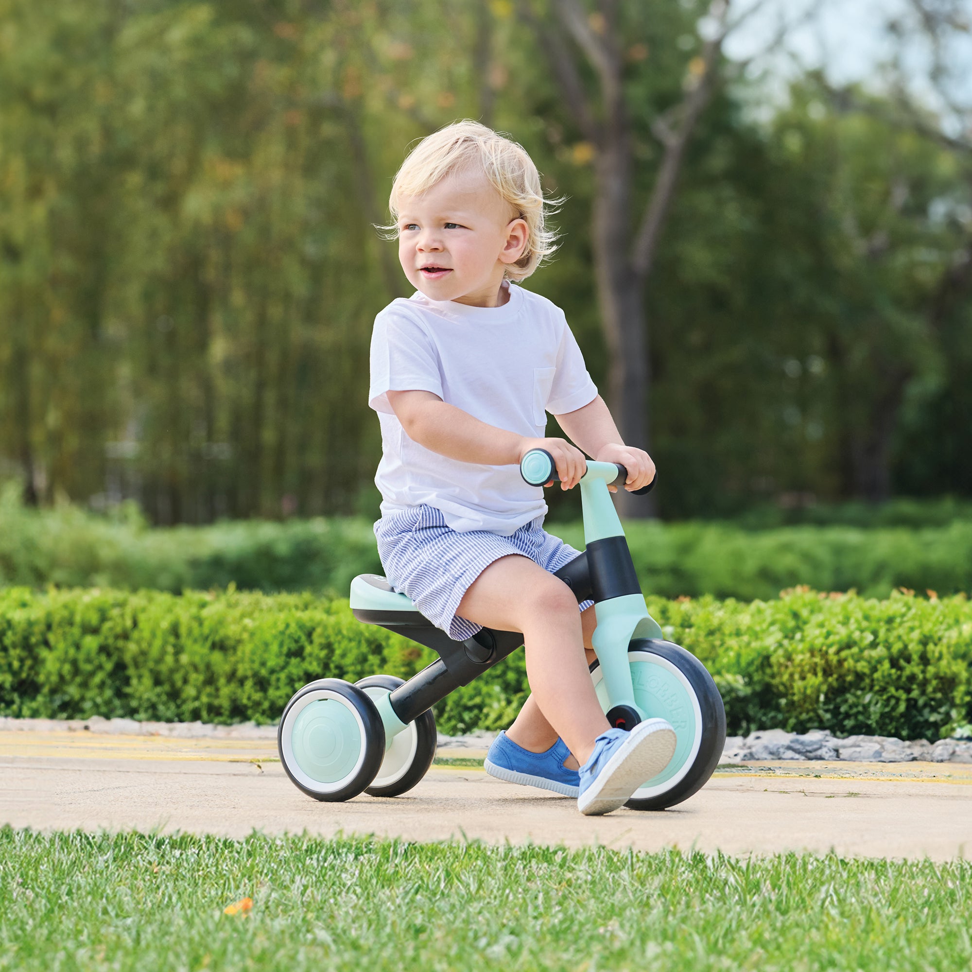Toddler riding a mint Learning Trike 2-in-1 with durable frame and ergonomic grips on a paved path outdoors